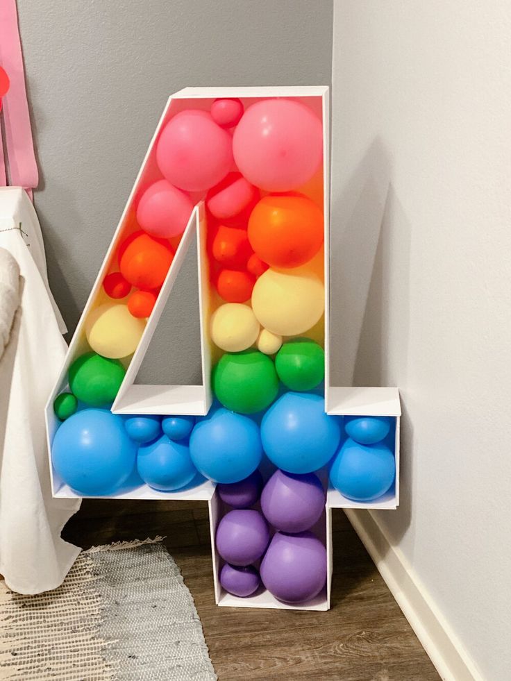 the number four is made out of balloons and sits on the floor next to a white vase
