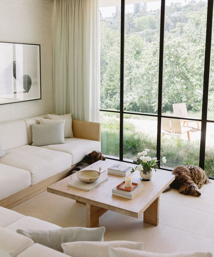 a living room filled with white furniture and large windows overlooking the trees in the distance