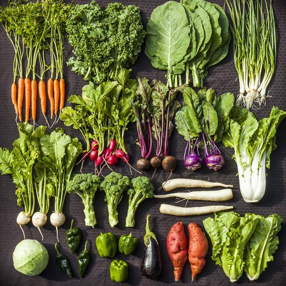 many different types of vegetables are laid out on a black tablecloth, including carrots, radishes, turnips, and broccoli