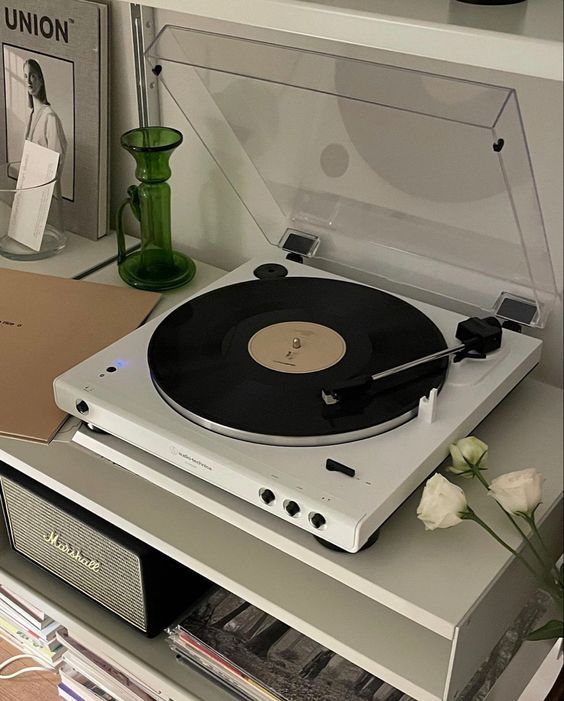 a record player sitting on top of a white shelf next to a vase with flowers