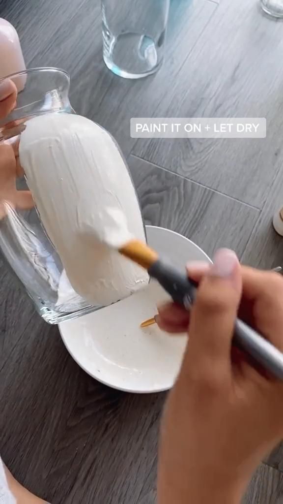 a person is painting a vase with white frosting on a plate while another person holds a paintbrush in their hand