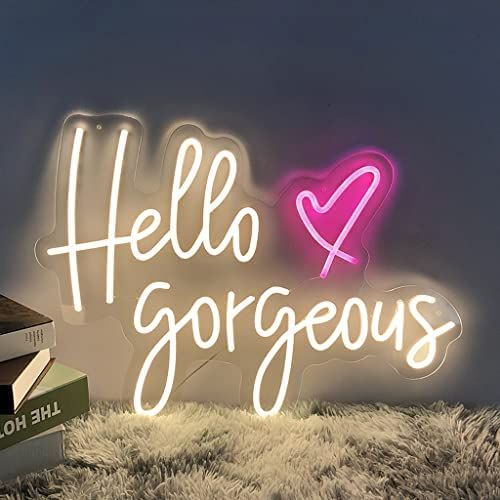 a stack of books sitting next to a neon sign that says hello gorgeous on it