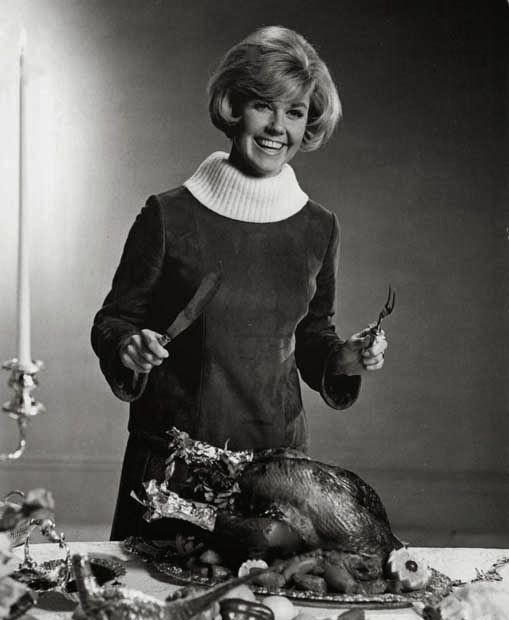 a woman standing in front of a turkey on a table with other foods and utensils