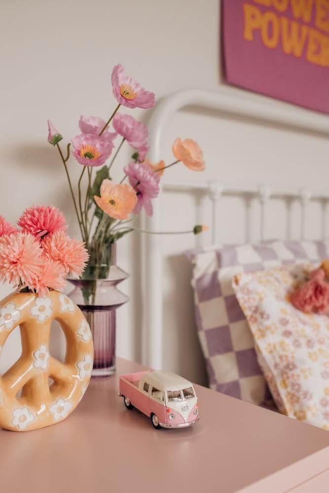 a pink and white bed with flowers in a vase next to a toy vw bus