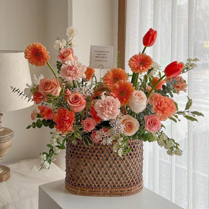 a basket filled with lots of flowers on top of a white table next to a window