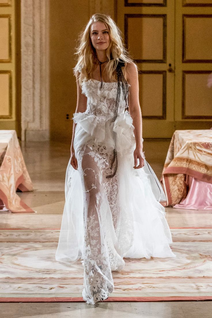 a model walks down the runway in a white gown with sheer panels and high slits