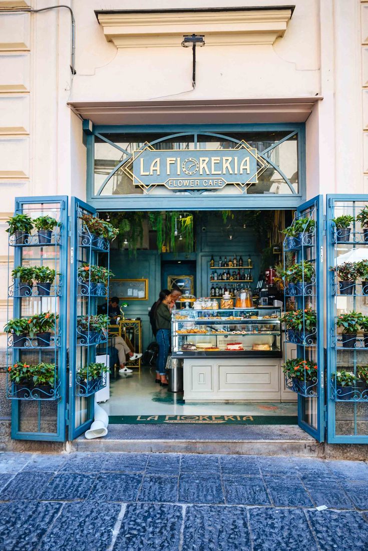 the front entrance to la feria coffee shop with potted plants in blue doors