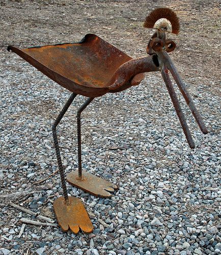 a metal bird with long legs standing on gravel