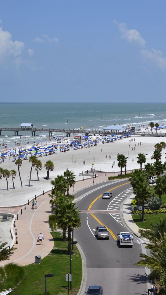 the beach is lined with palm trees and blue umbrellas as well as cars driving down the road