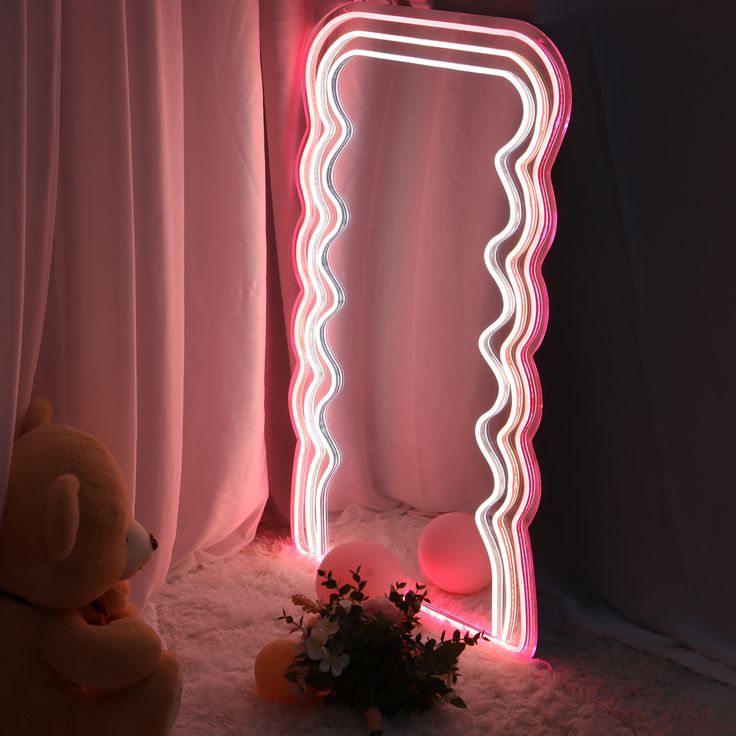 a teddy bear sitting in front of a pink lighted mirror