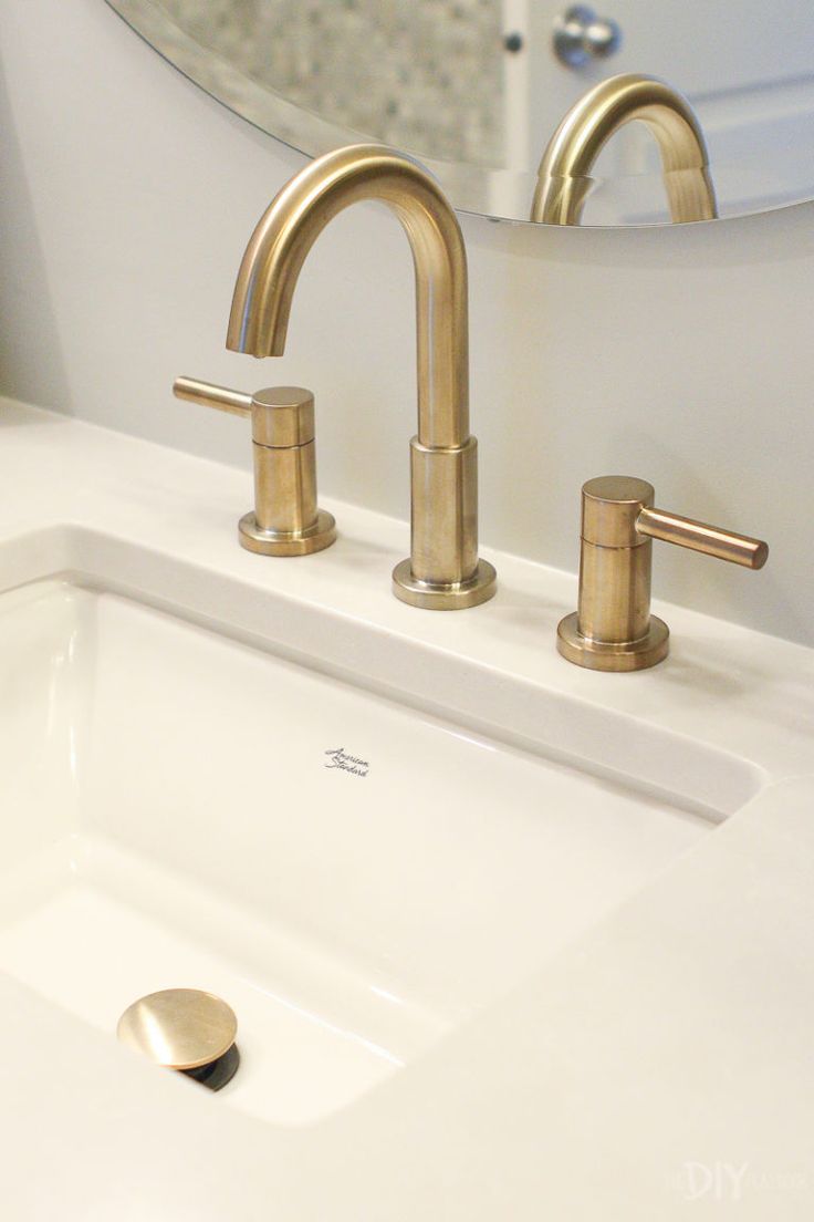a bathroom sink with two brass faucets and a mirror above it, in front of a white toilet