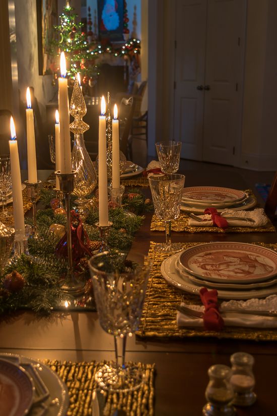 a dining room table set for christmas with lit candles and place settings on the table