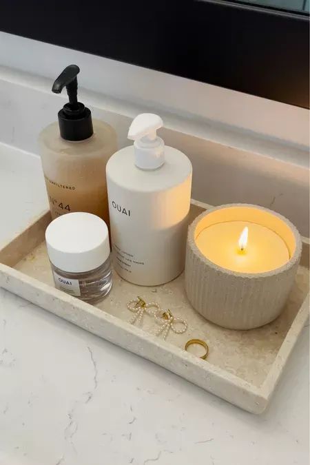 a bathroom sink with soap, lotion bottle and candle on the tray next to it