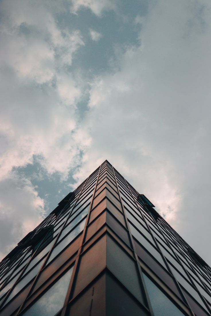 looking up at the side of a tall building with windows and sky in the background