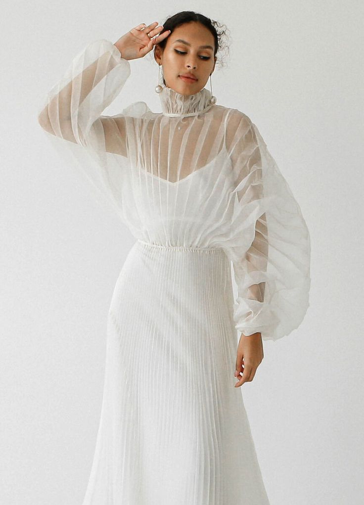 a woman wearing a white dress with sheer sleeves