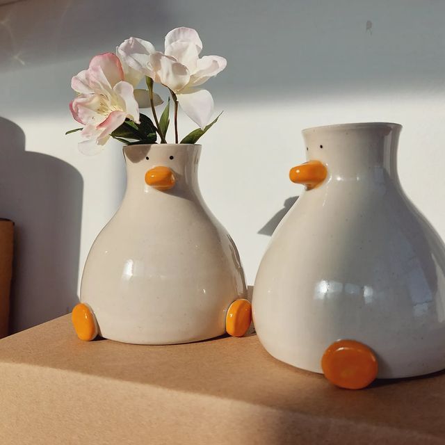 two white vases with flowers in them sitting on a cardboard box next to each other