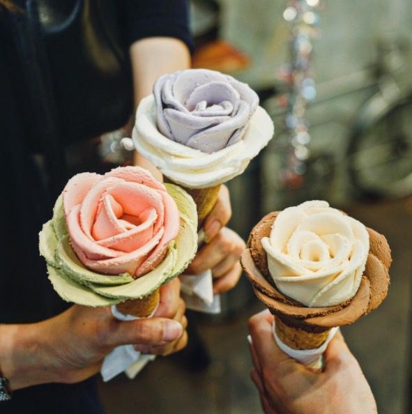 three people holding ice cream cones with flowers on them and one is frosting the other
