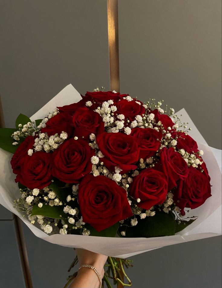 a bouquet of red roses with baby's breath in the center is being held by someone