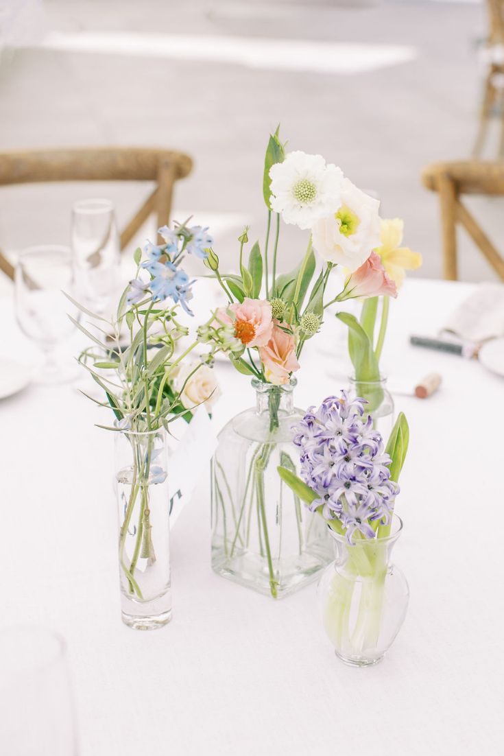three vases filled with flowers sitting on top of a white tablecloth covered table