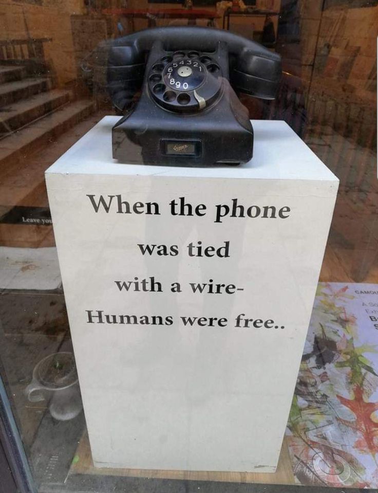 an old phone sitting on top of a sign that says, when the phone was tied with a wire humans were free