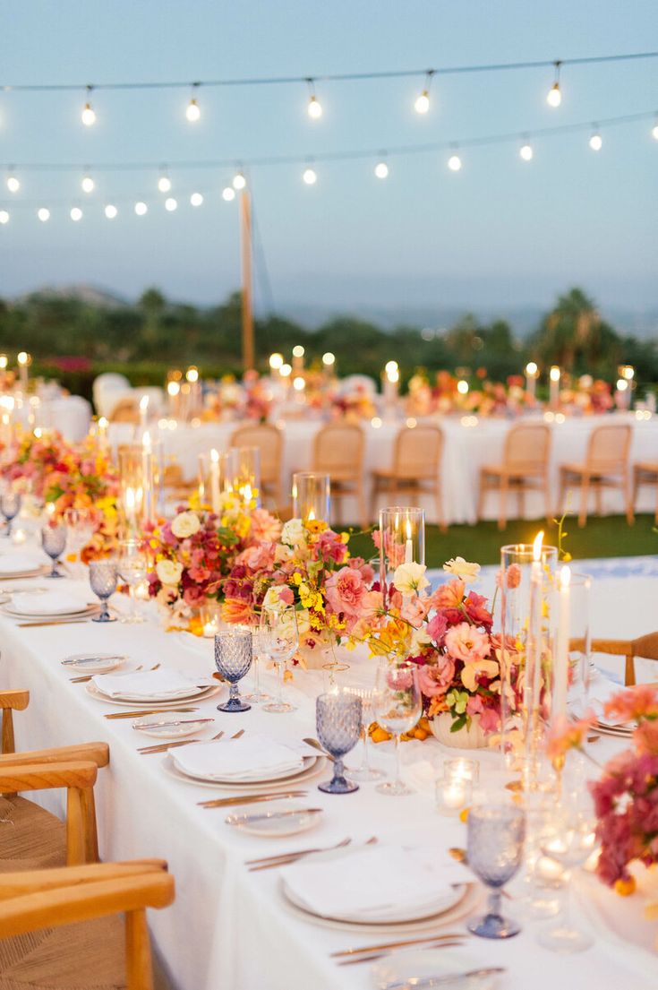 a long table is set with flowers and candles for an outdoor wedding reception at dusk