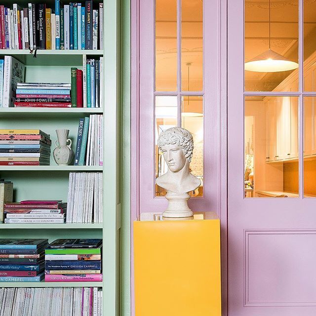 a book shelf with books and a bust on it in front of a pink door