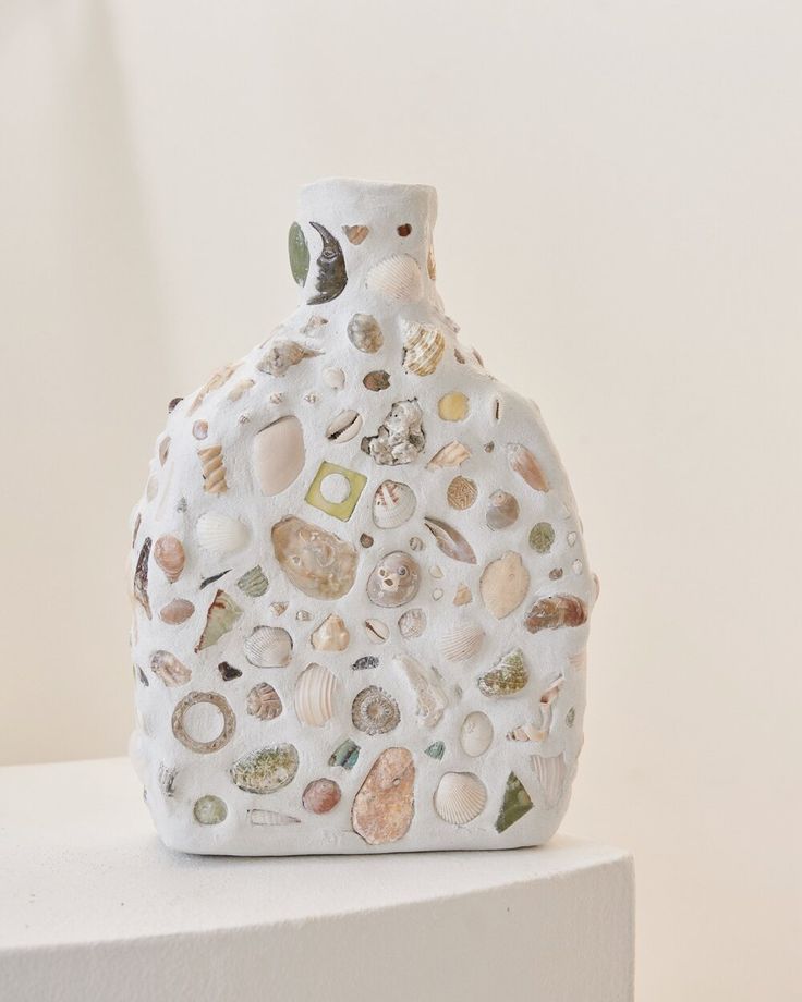 a white vase with shells and seashells on it sitting on a shelf next to a wall