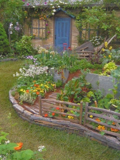 the garden is full of flowers and plants, including an old wooden fence with a blue door