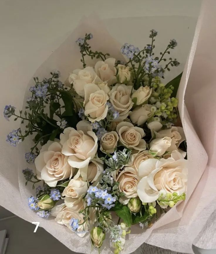 a bouquet of white roses and blue flowers in a paper wrapper on a table