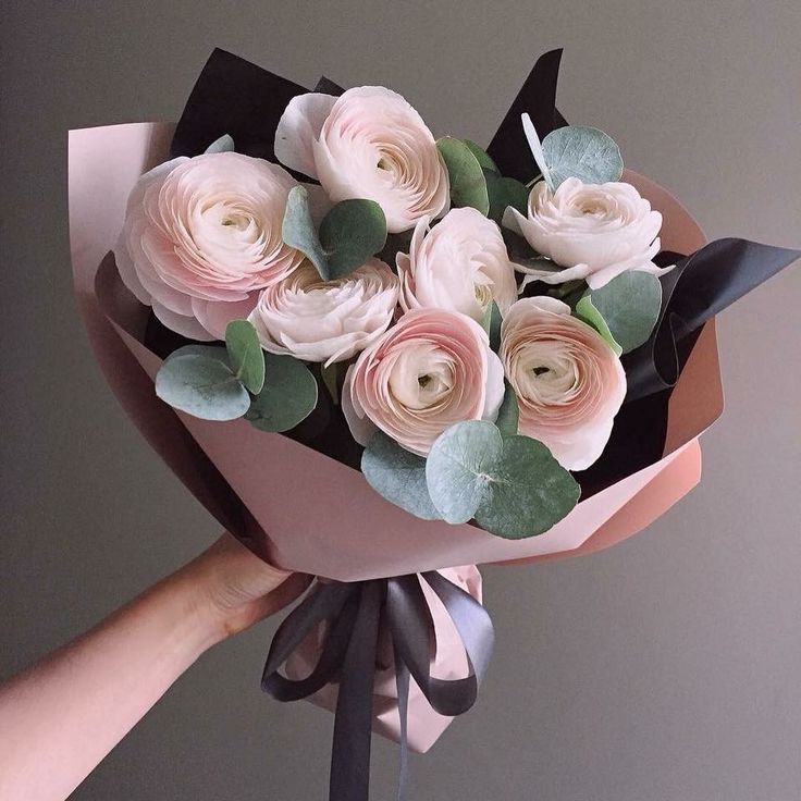 a hand holding a bouquet of pink roses with green leaves on the top and bottom