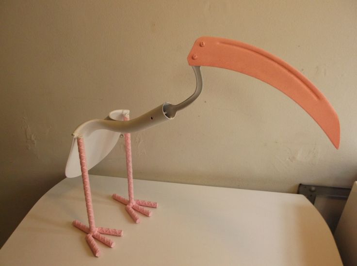 a pink and white bird with long legs on top of a table next to a lamp