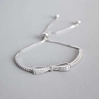 a silver bracelet with a bow on the clasp and beads around it, sitting on a gray surface