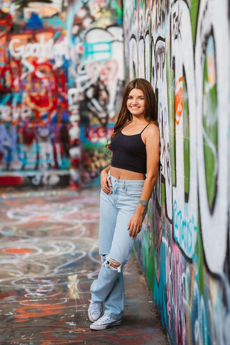 a young woman leaning against a wall with graffiti on it and smiling at the camera