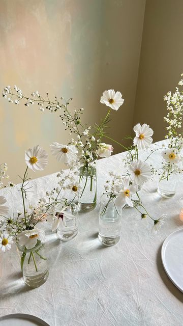 several vases filled with white flowers sitting on a table next to plates and candles