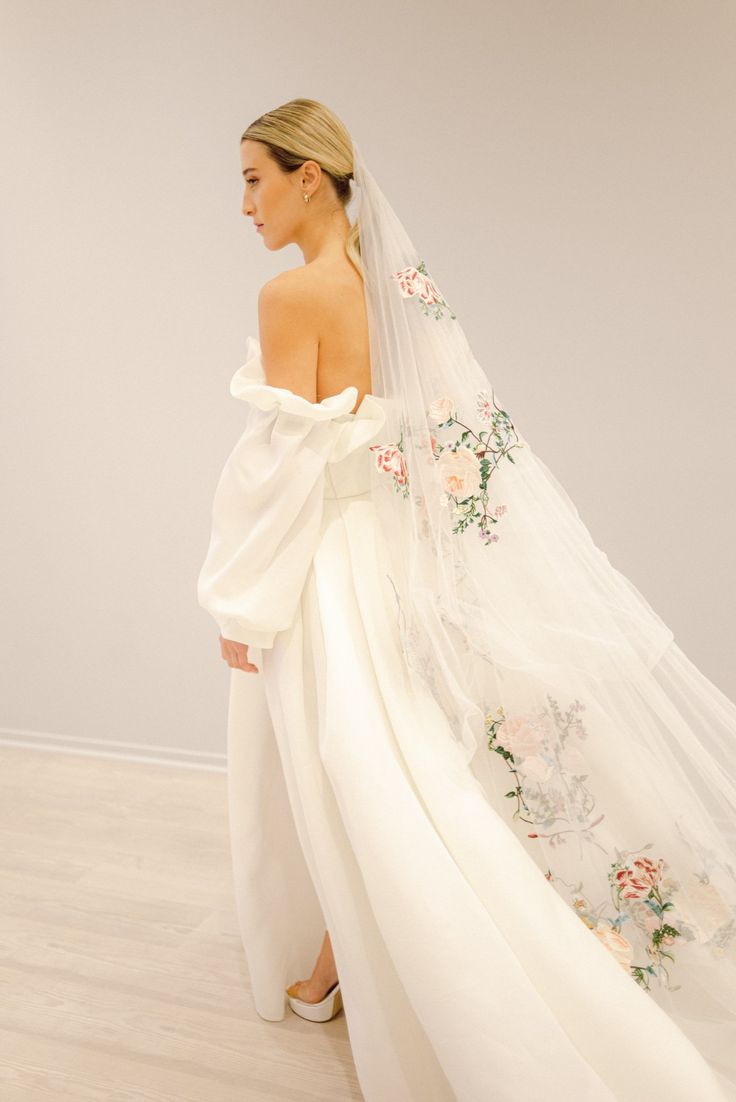 a woman wearing a wedding dress with flowers on the side and veil over her shoulder