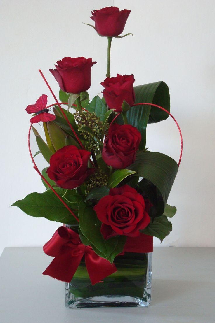 a vase filled with red roses and greenery