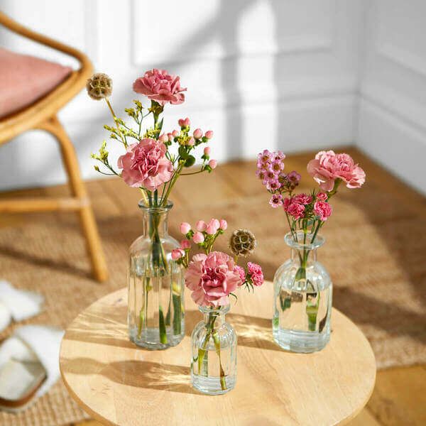 three vases with pink flowers are sitting on a round table in front of a chair