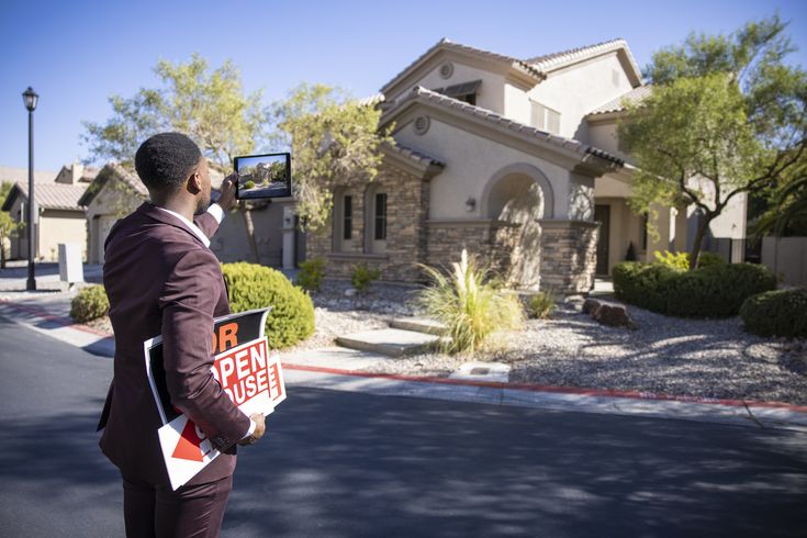 a man standing in front of a house with a real estate sign on his hand