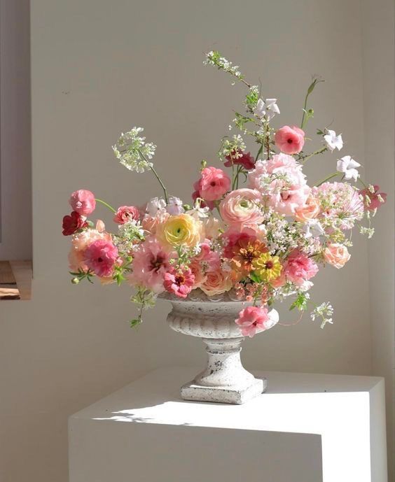 a vase filled with lots of pink and white flowers on top of a table next to a window