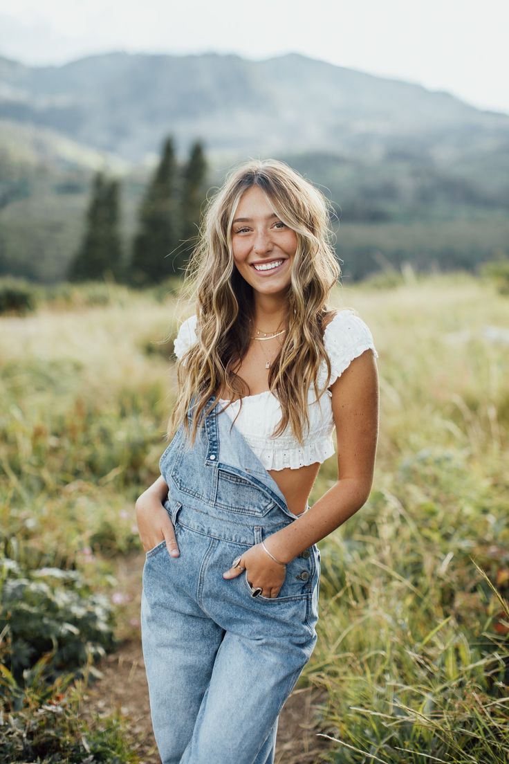 a smiling woman in overalls standing on a hill