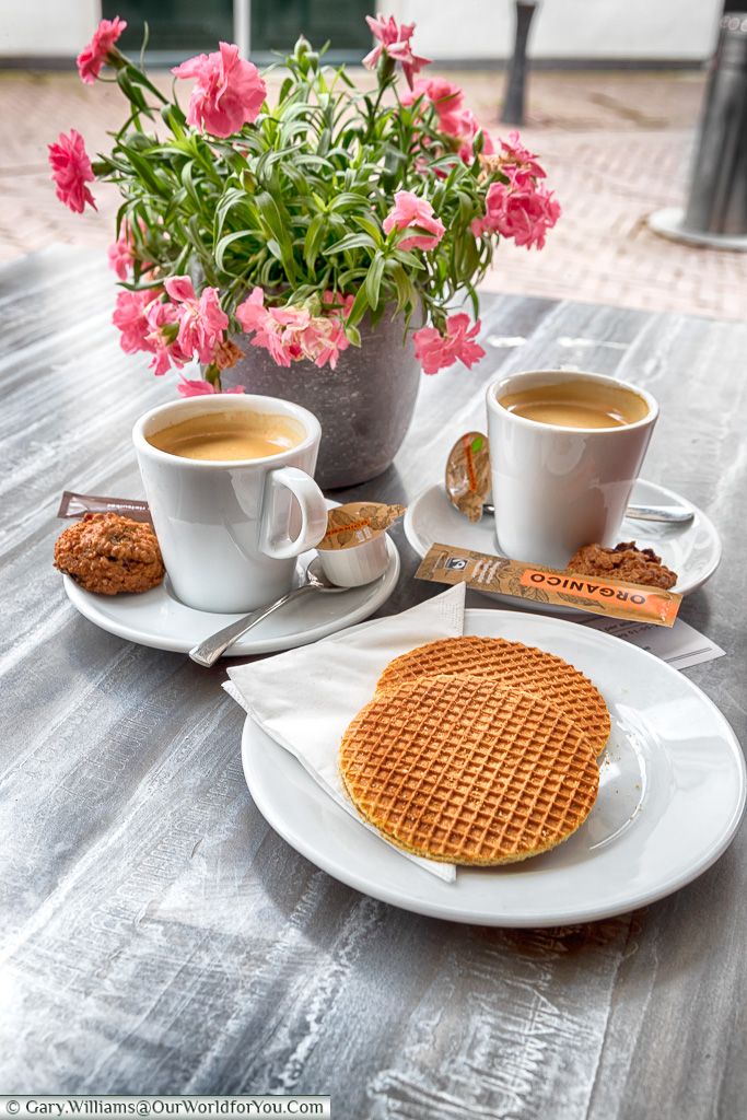 two cups of coffee and some waffles on a table with flowers in the background