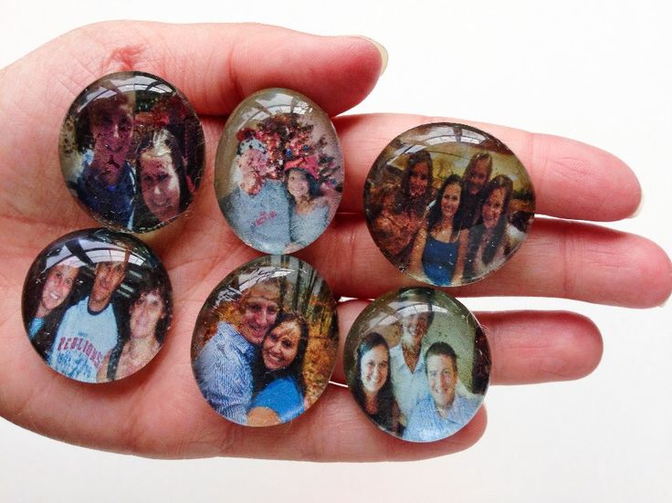 a hand holding four glass magnets with pictures on them