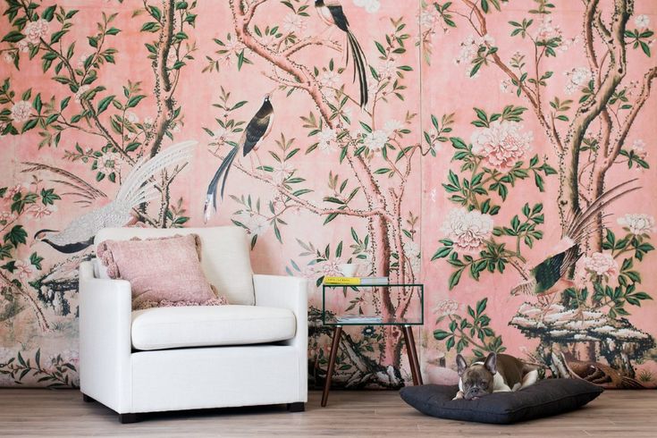 a living room with pink wallpaper and birds on the tree mural behind a white chair