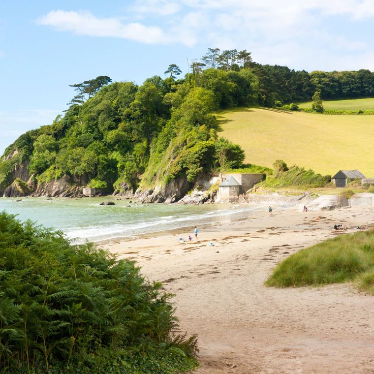 a sandy beach next to the ocean with people on it and green hills in the background