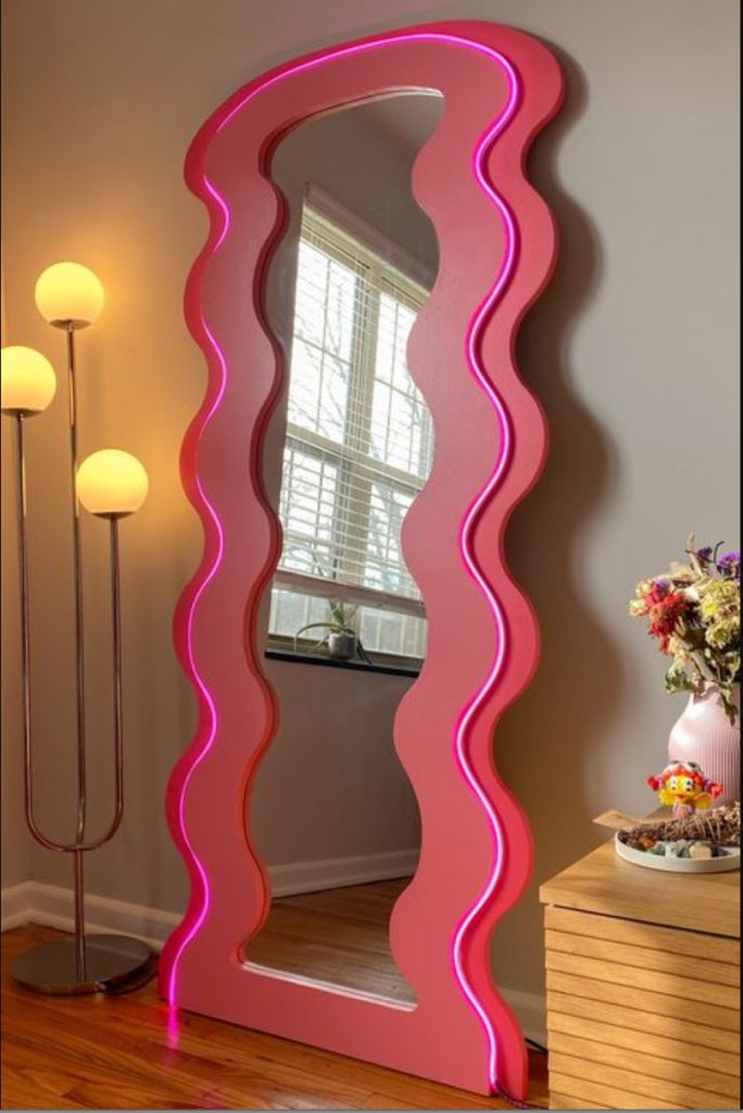 a large pink mirror sitting on top of a wooden floor next to a table and lamp