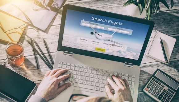 a man is working on his laptop with the search flights page displayed on it, surrounded by other office supplies