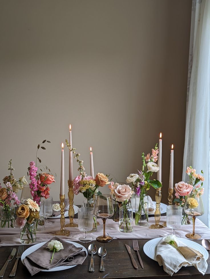 the table is set with candles and flowers in vases, plates and silverware