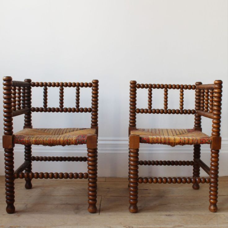 two wooden chairs sitting next to each other on a hard wood floored floor in front of a white wall