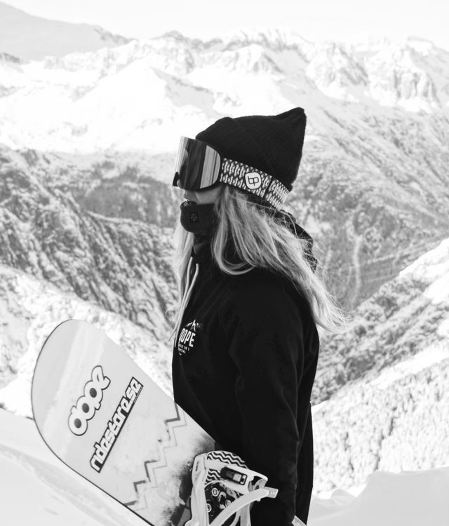 black and white photograph of a woman holding a snowboard on top of a mountain