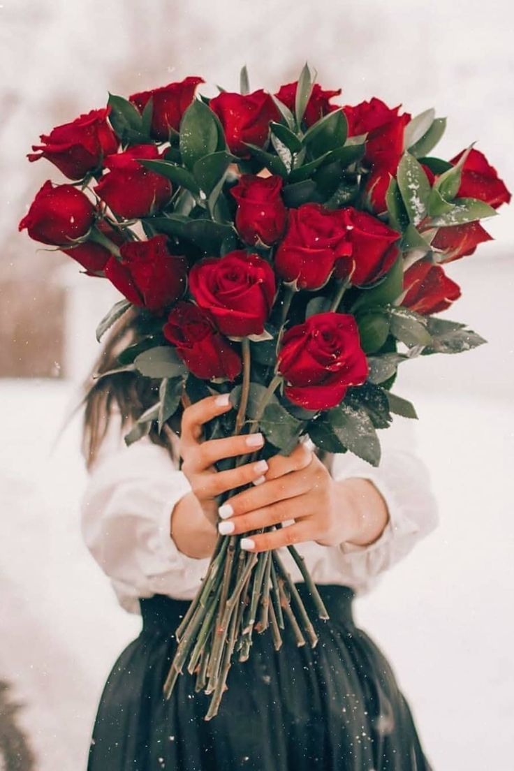 a woman holding a bunch of red roses in her hands while standing in the snow